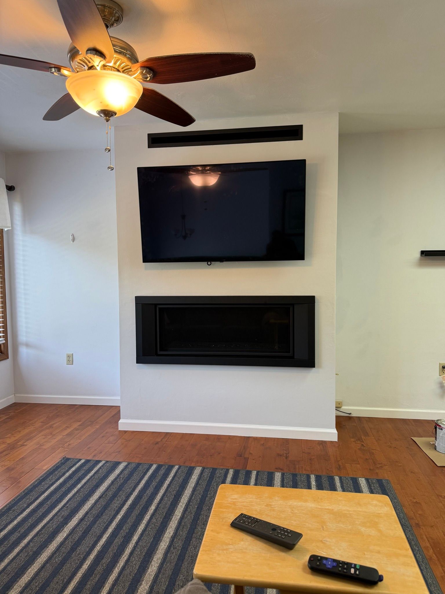 Living room with a mounted TV above an electric fireplace on a white wall.