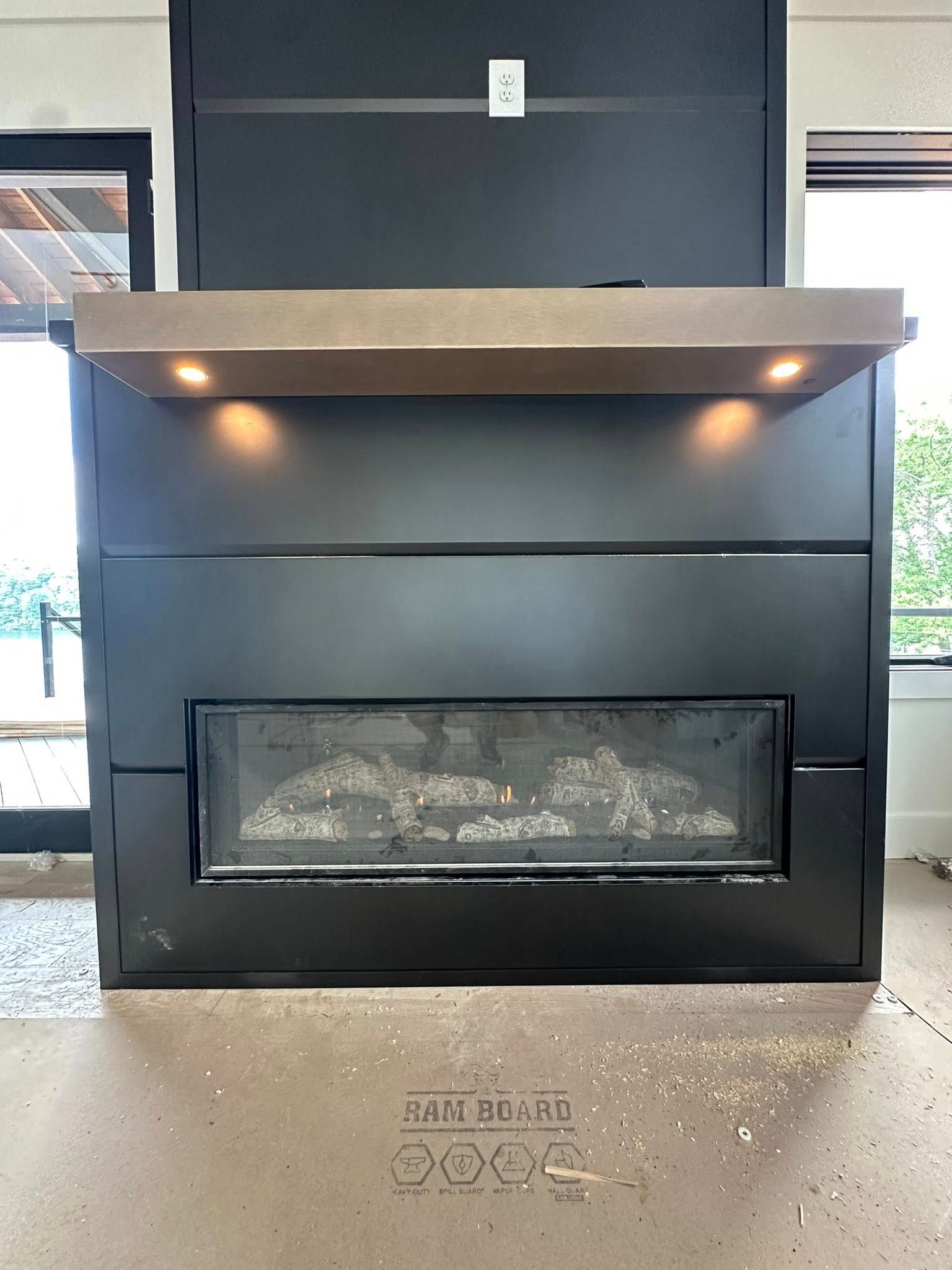 Black fireplace with a concrete-look mantel, with two lights.