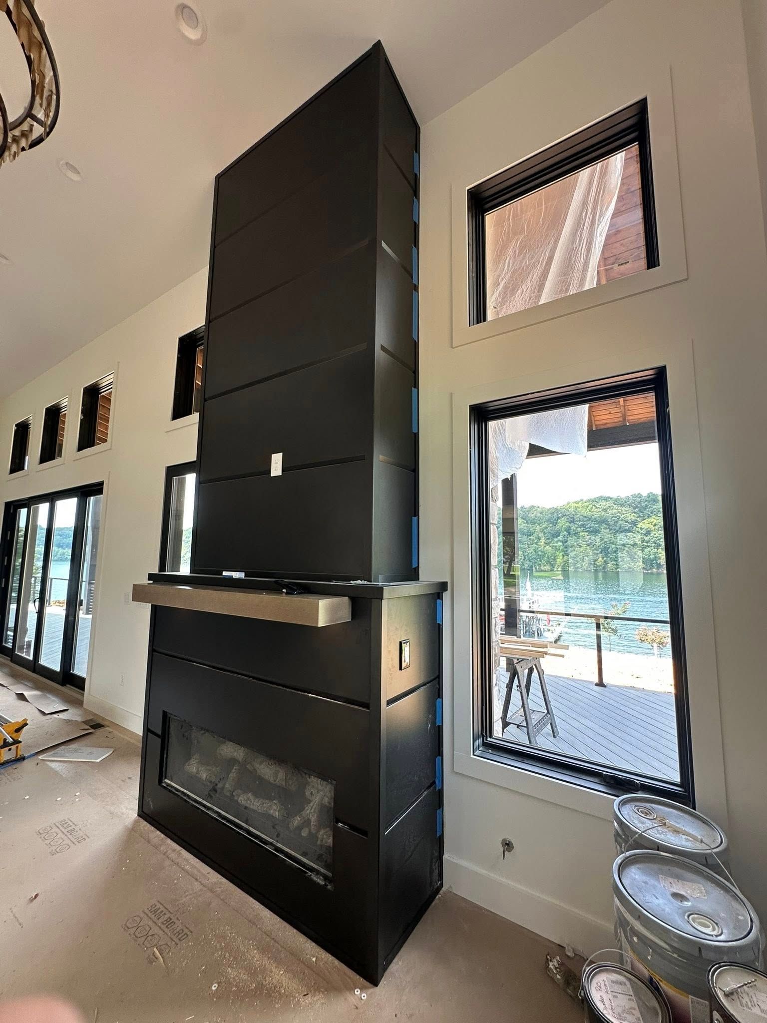 Black modern fireplace in a room with white walls and windows overlooking water.