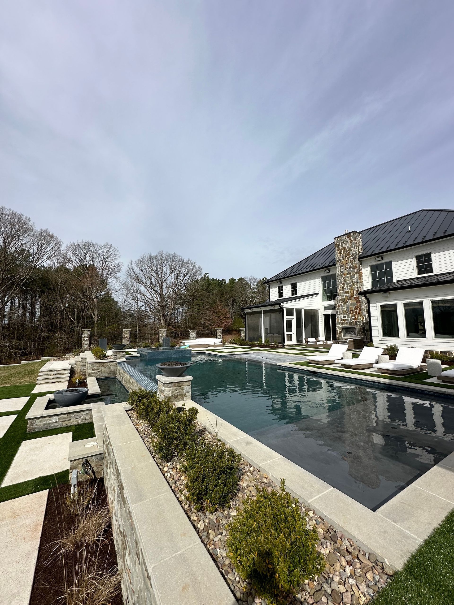 Luxury home with a rectangular swimming pool, landscaping, and a cloudy sky backdrop.