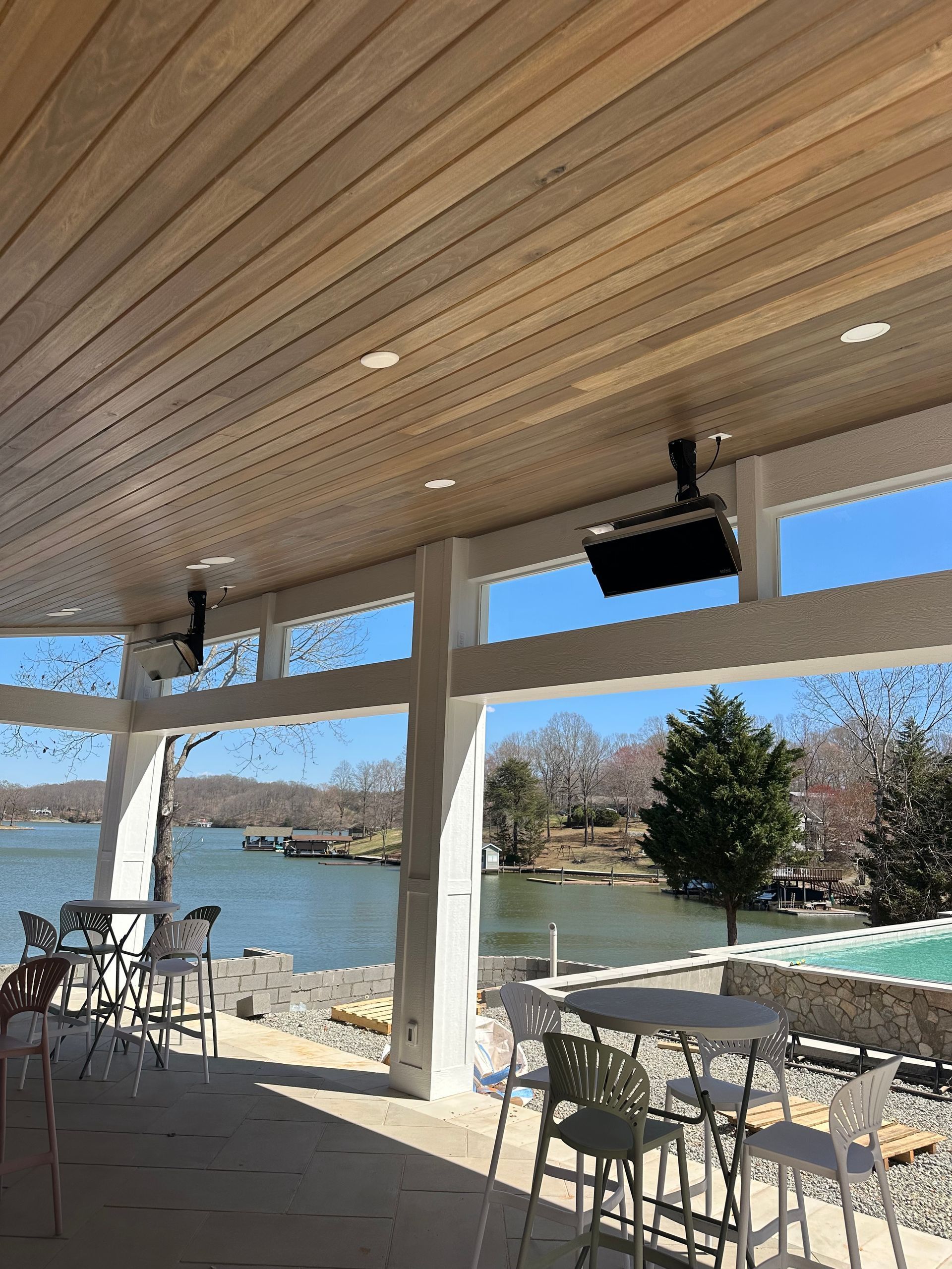 Outdoor patio with lake view, tables, chairs, and speakers on the ceiling.