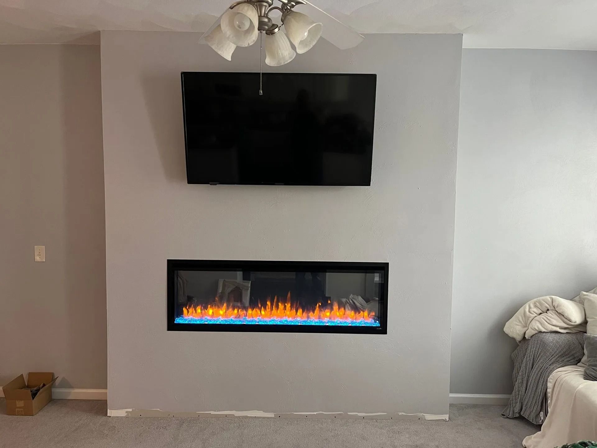 Gray wall with a mounted TV above an electric fireplace; a ceiling fan is visible.