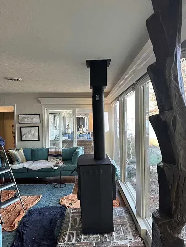 Black fireplace with vertical chimney in living room with a turquoise couch and windows.