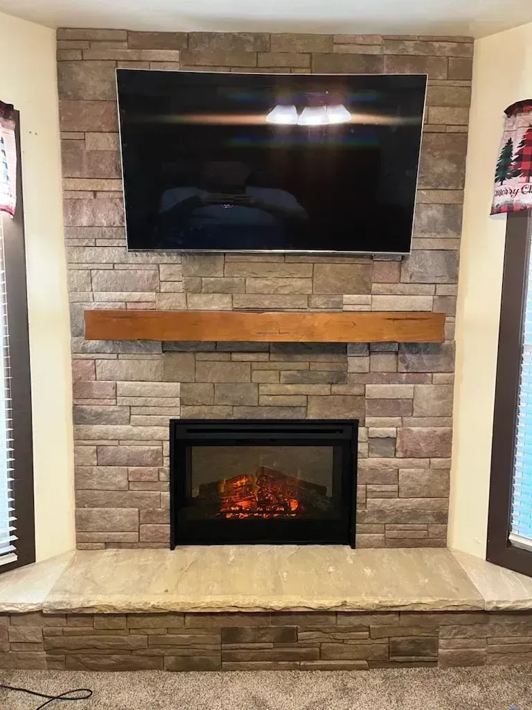 Stone fireplace with mounted TV, wooden mantel, and electric fire.