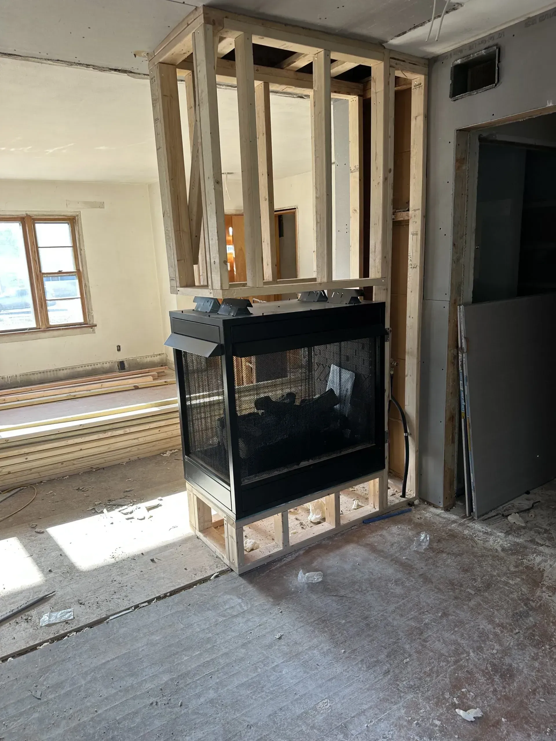 Framed fireplace in a partially constructed room. Wooden framework surrounds a black fireplace.