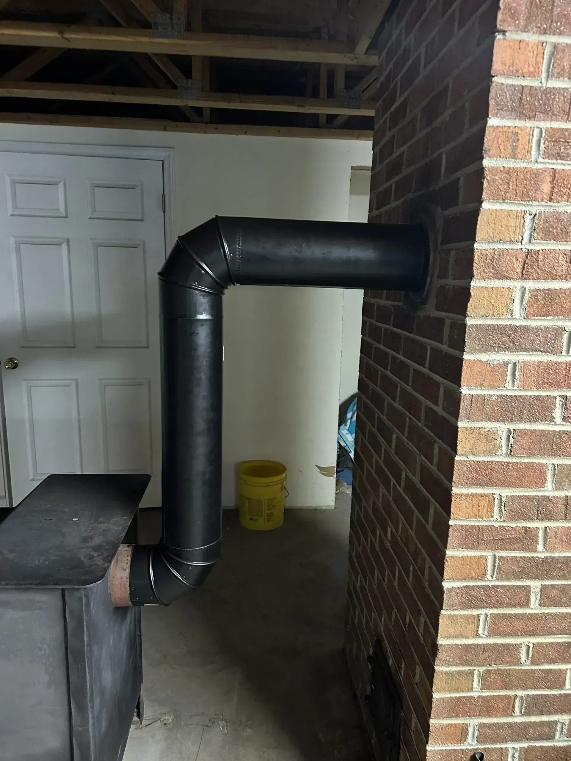Black stovepipe connecting a wood stove to a brick chimney in a basement.