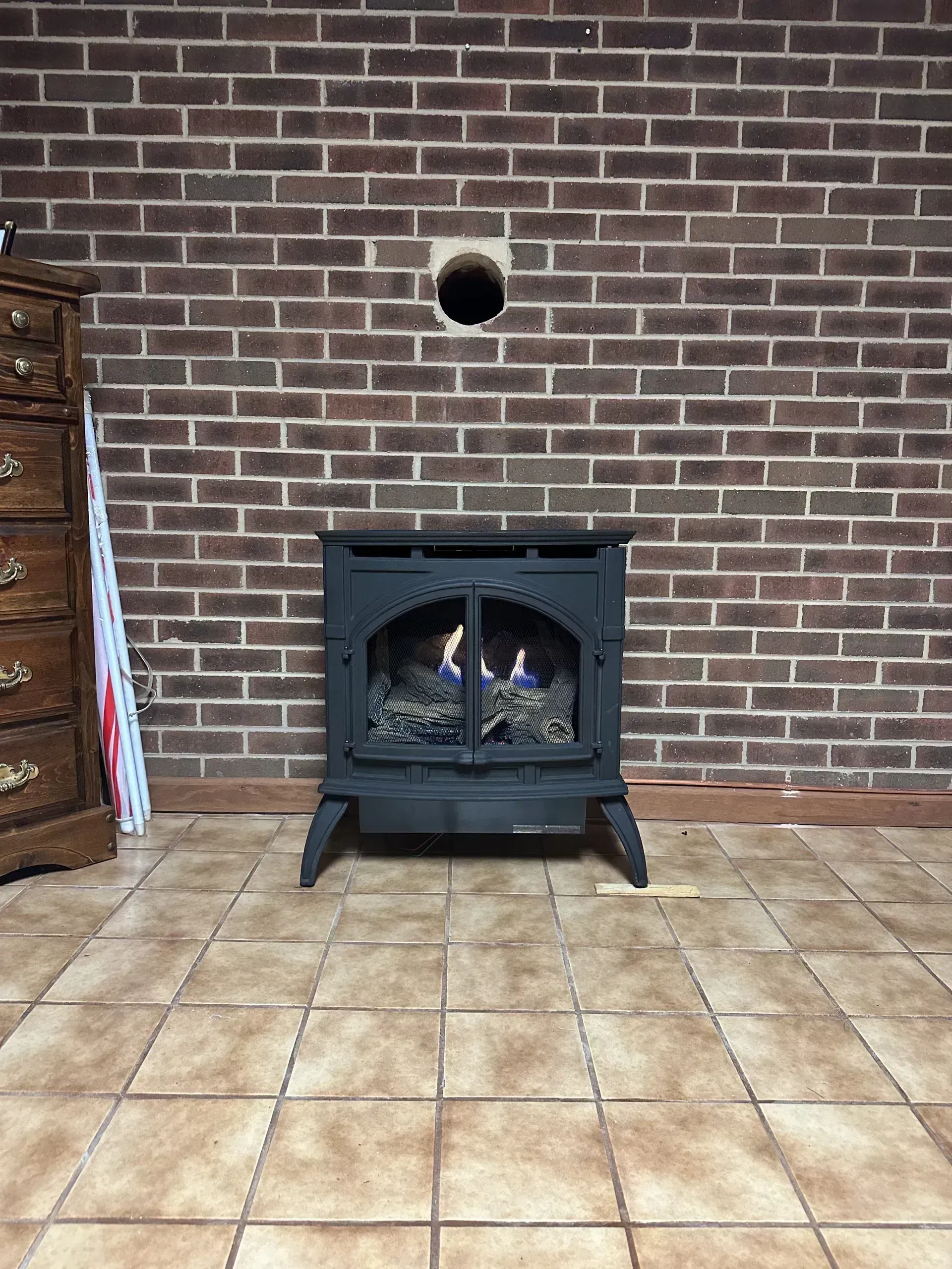 A black gas fireplace against a brick wall, with blue flames visible.