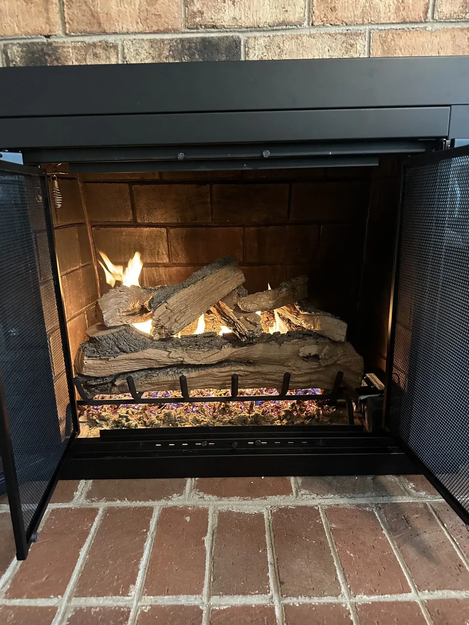 Fireplace with burning gas logs, brick interior, black screen and frame, open.