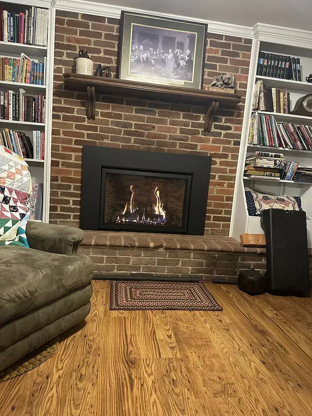 Fireplace with black surround, flanked by bookshelves, brick wall, rug on wood floor.