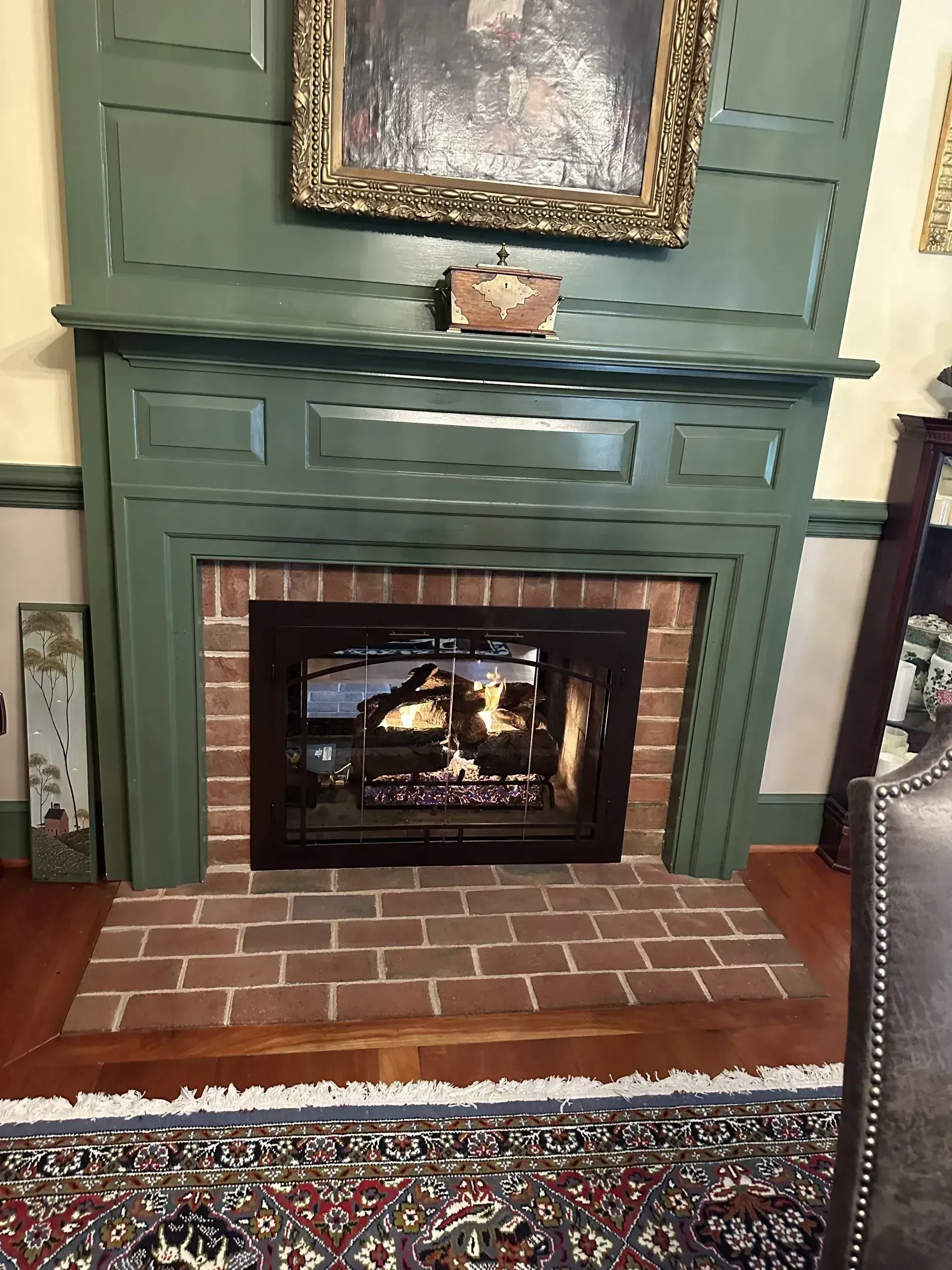 Green-painted fireplace with a brick surround, beneath a portrait and a decorative wall.