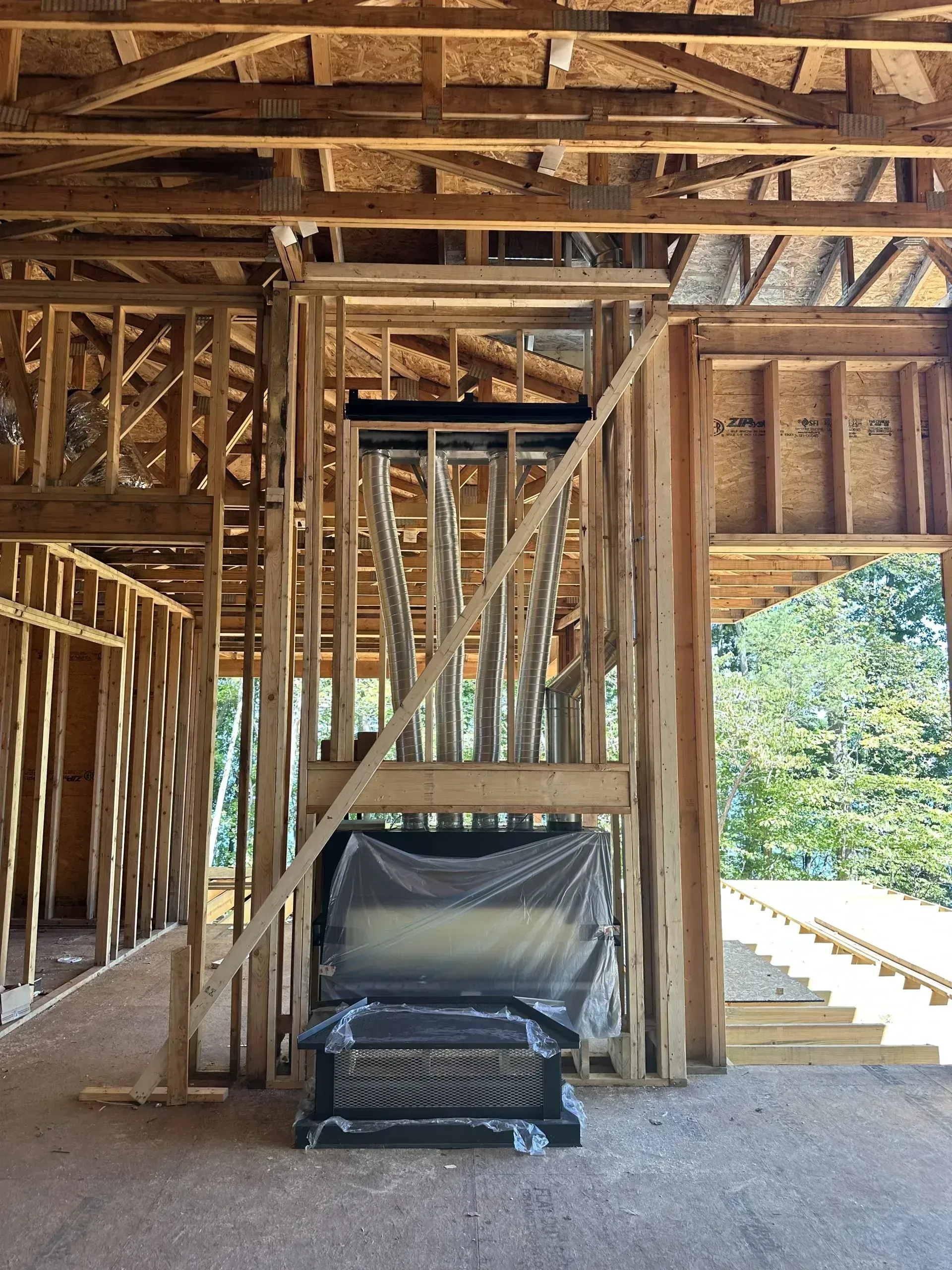 Wooden-framed house under construction. Fireplace covered in plastic. Staircase to the right. Interior view.