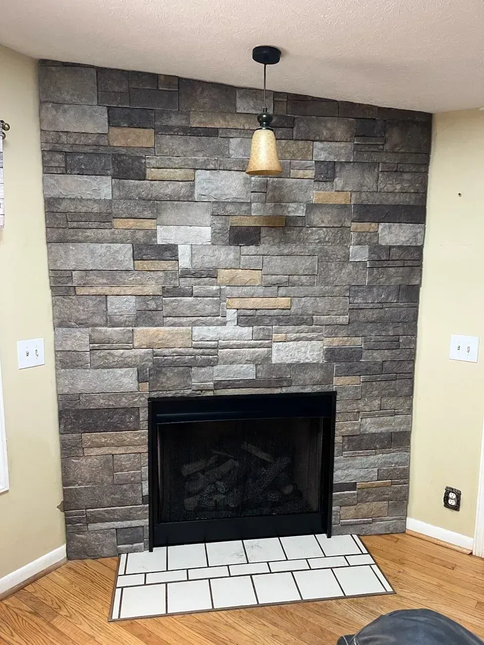 Stone fireplace with a black insert, a light fixture, and tile on the floor.
