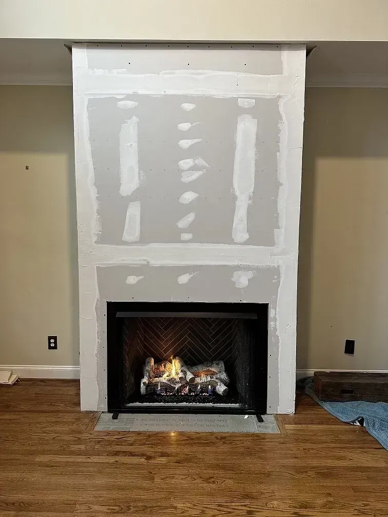 Fireplace with unfinished drywall surround; gas fire burning. Hardwood floor.