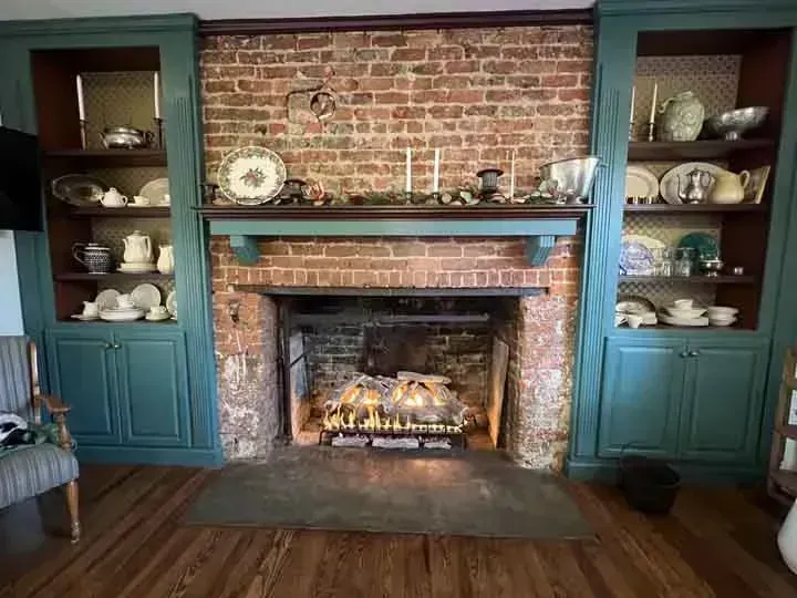 Fireplace with teal cabinets, brick wall, and various dishware.
