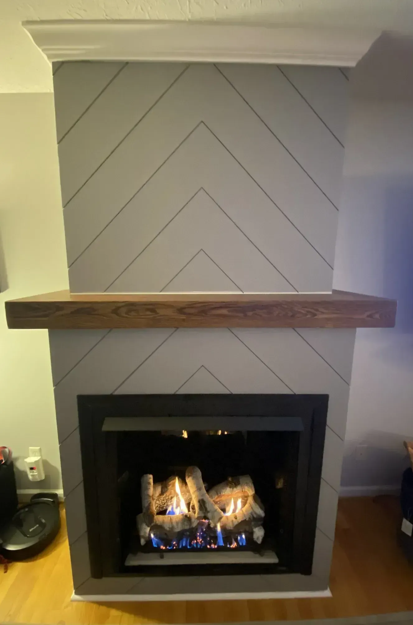 A fireplace with a gray chevron pattern surround, a wooden mantel, and a lit fire.