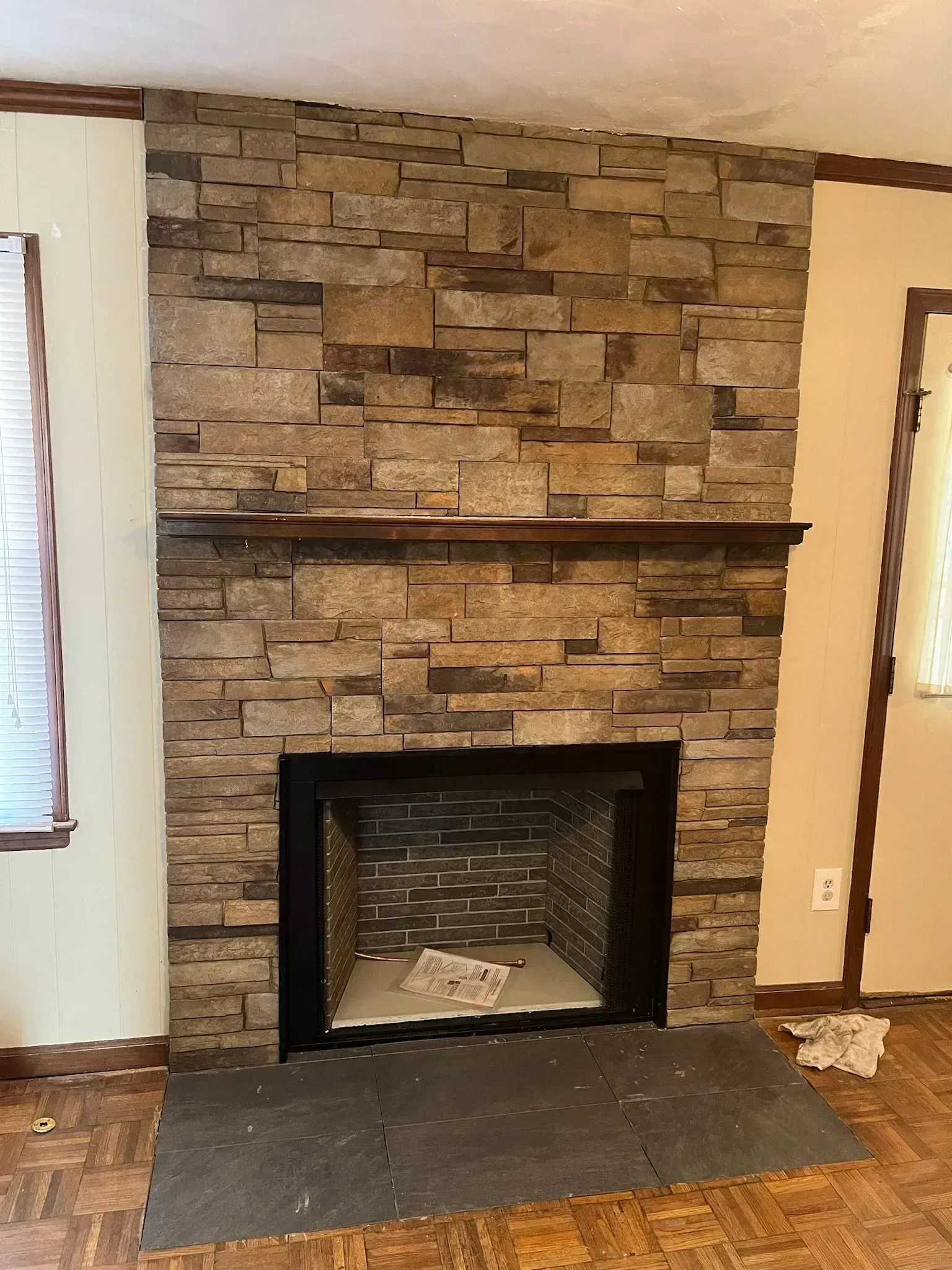 Stone-covered fireplace with a dark mantel, black firebox, and a dark stone hearth in a room.