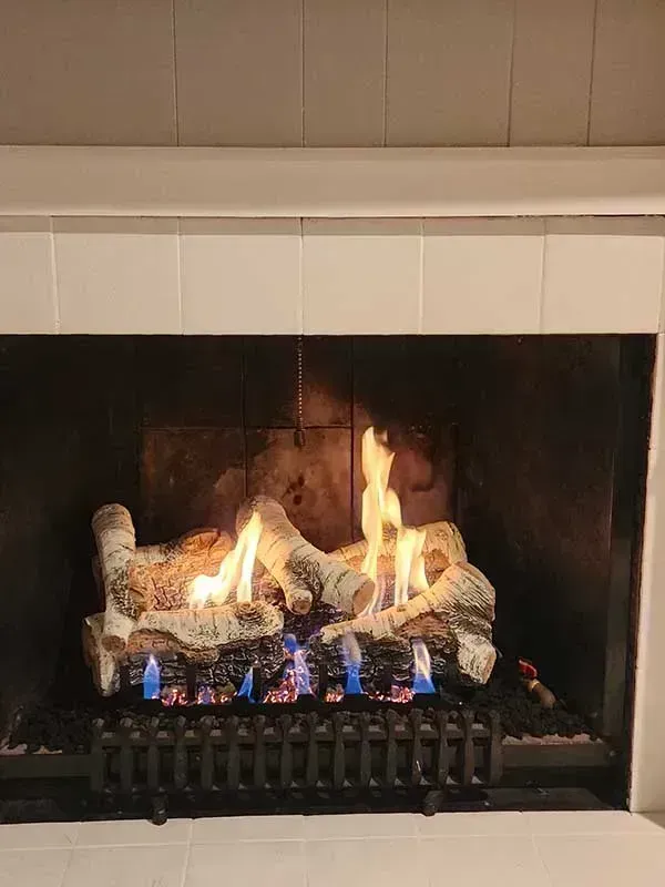 Fireplace with burning gas logs, framed by a white mantel and white tiled wall.