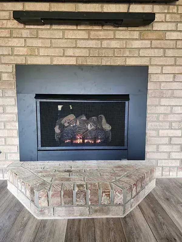 Brick fireplace with a black surround, lit gas logs, and a brick hearth.