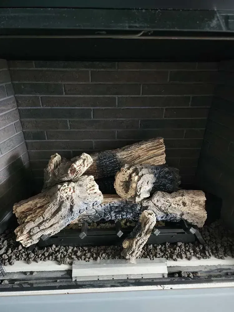 Gas fireplace with ceramic logs, set against a dark brick background.