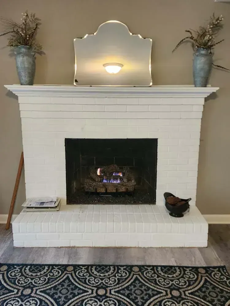 White painted brick fireplace with lit flames, mirror, and decorations.