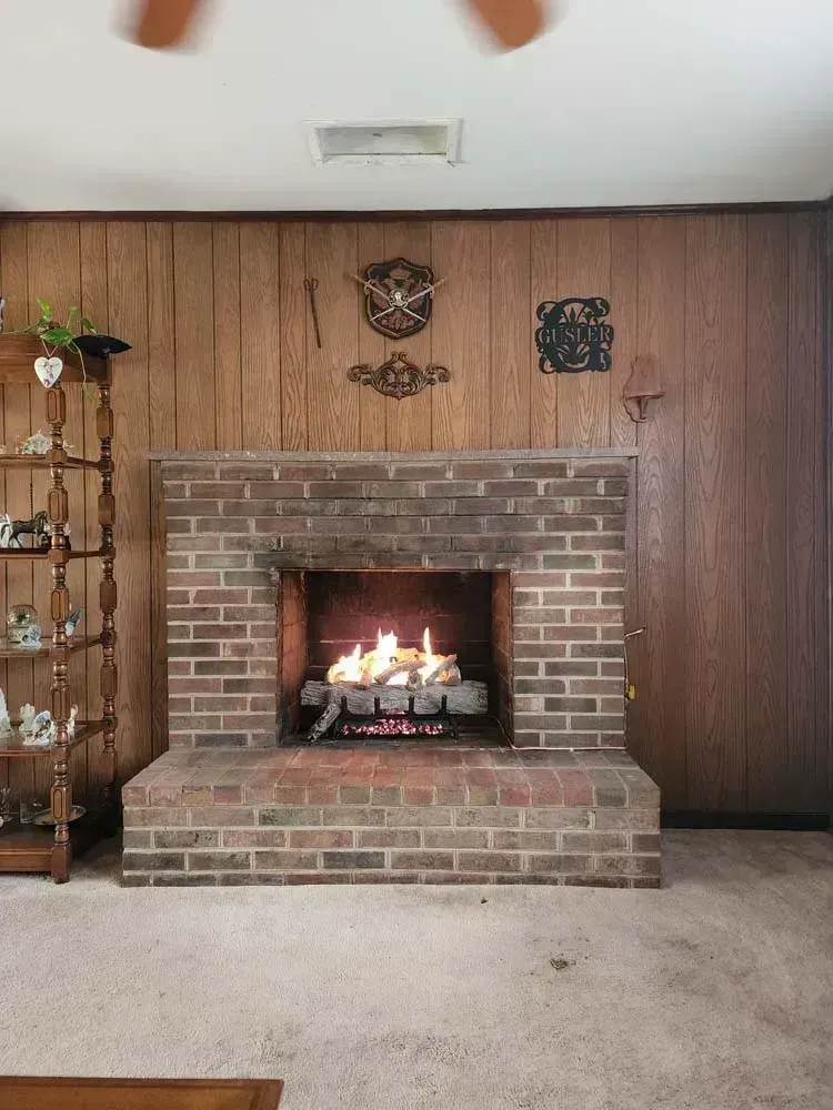 Brick fireplace with a fire burning, set against wood paneling.