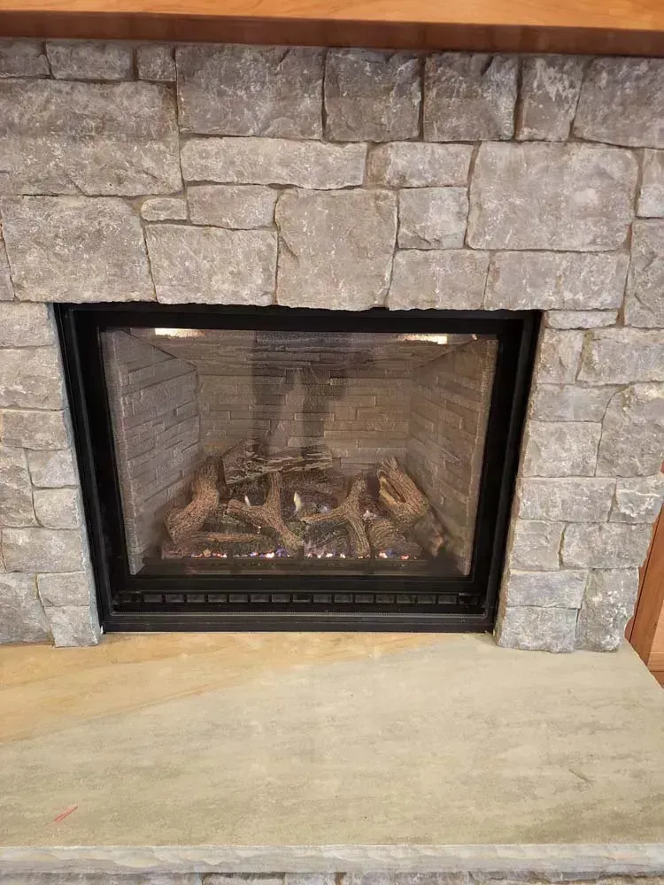 Fireplace with stone surround, black frame, and gas logs.