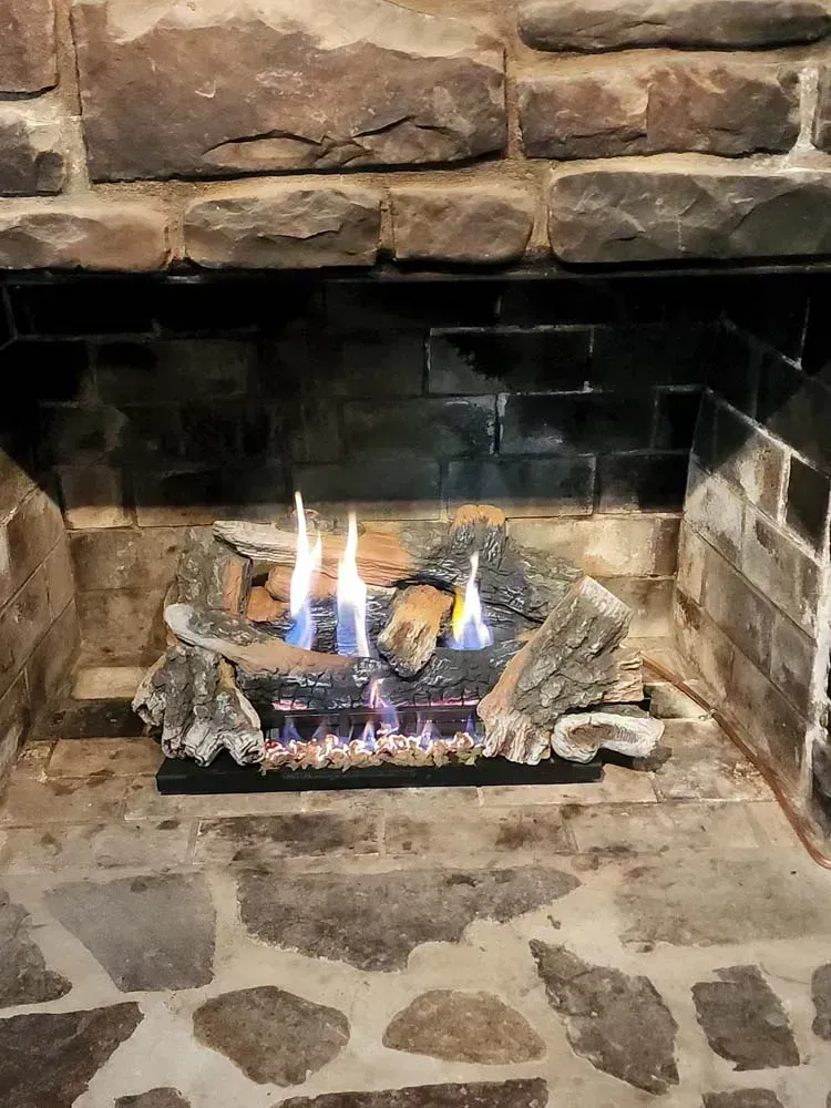Fireplace with gas logs burning, set in a stone and brick hearth.