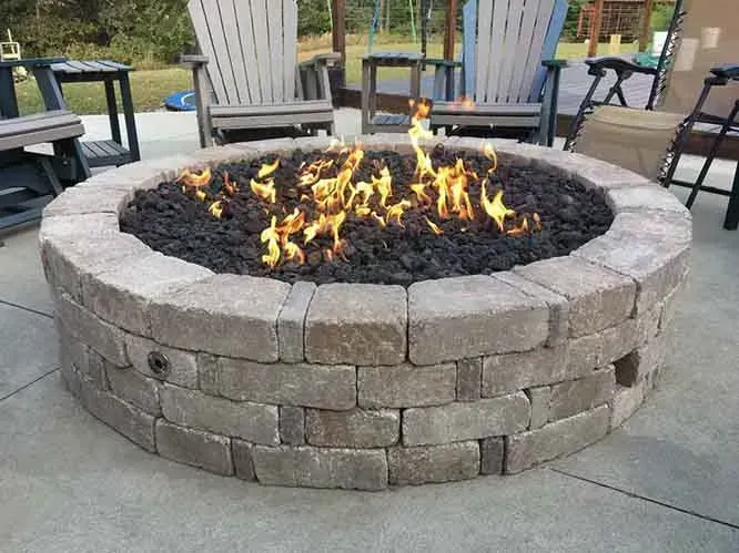 Stone fire pit with burning flames, surrounded by lava rocks and patio furniture.