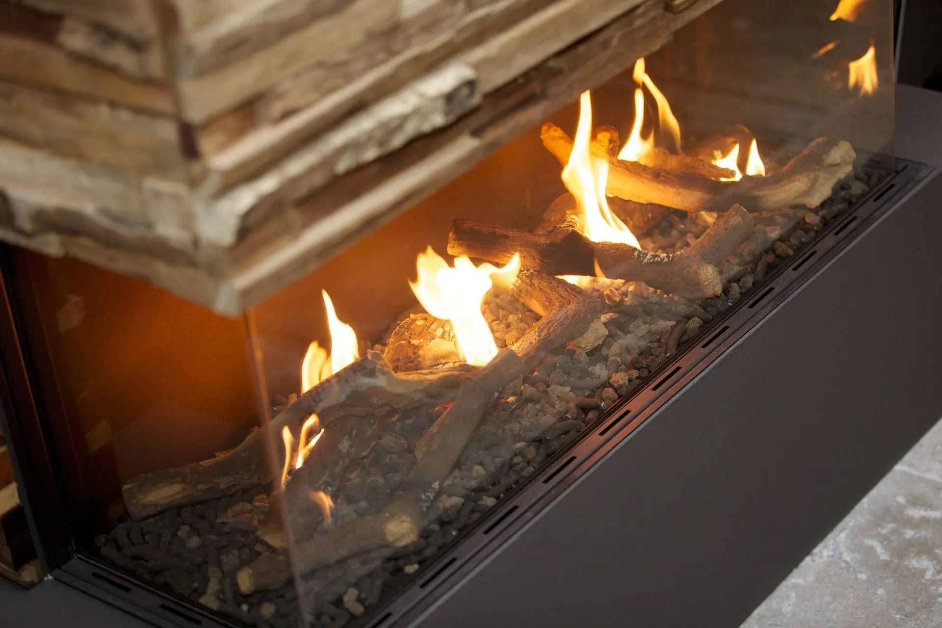 Fireplace with burning logs behind glass, with a stone structure above.