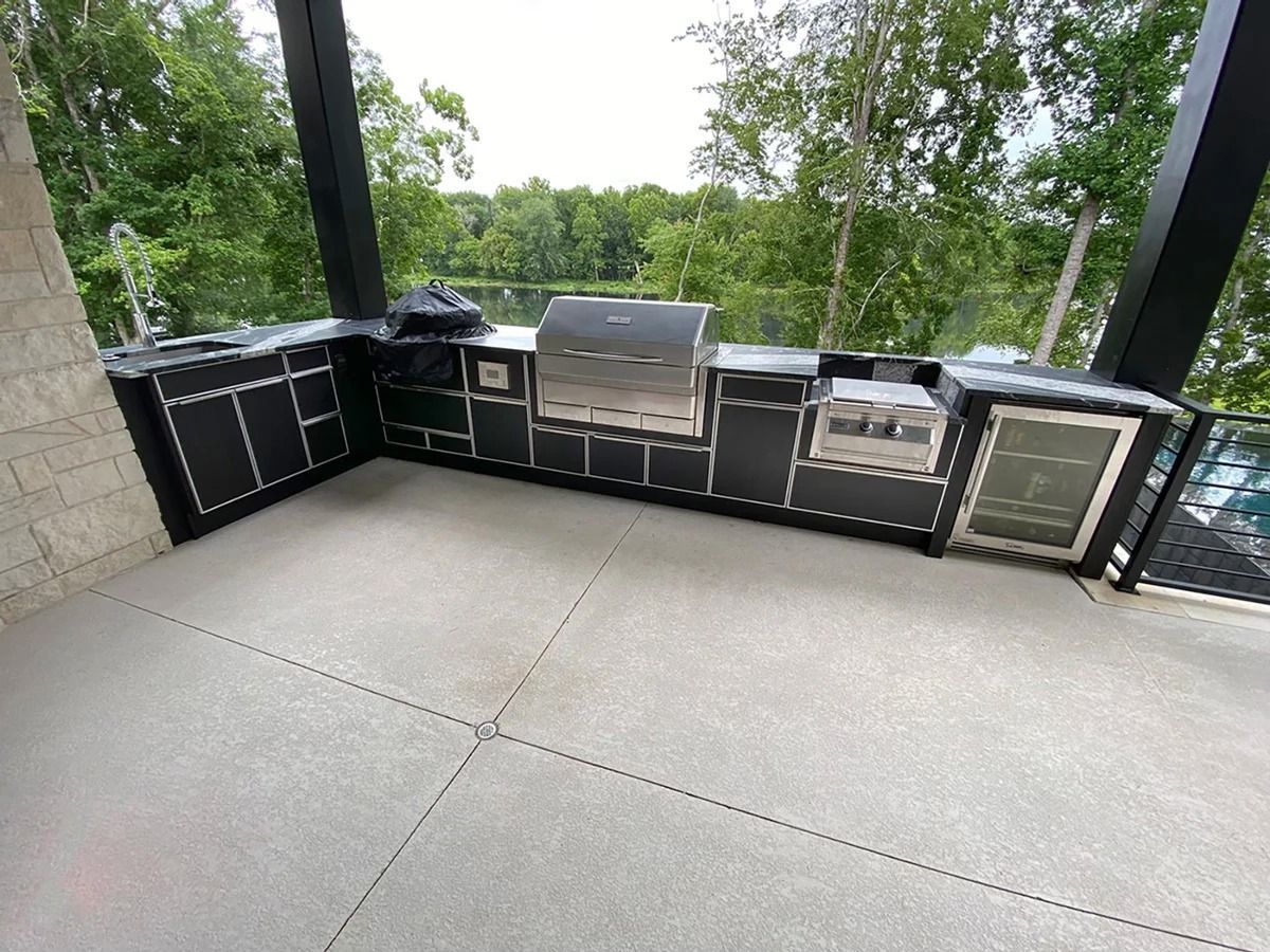 Outdoor black kitchen with grill, fridge, and countertop overlooking a lake.