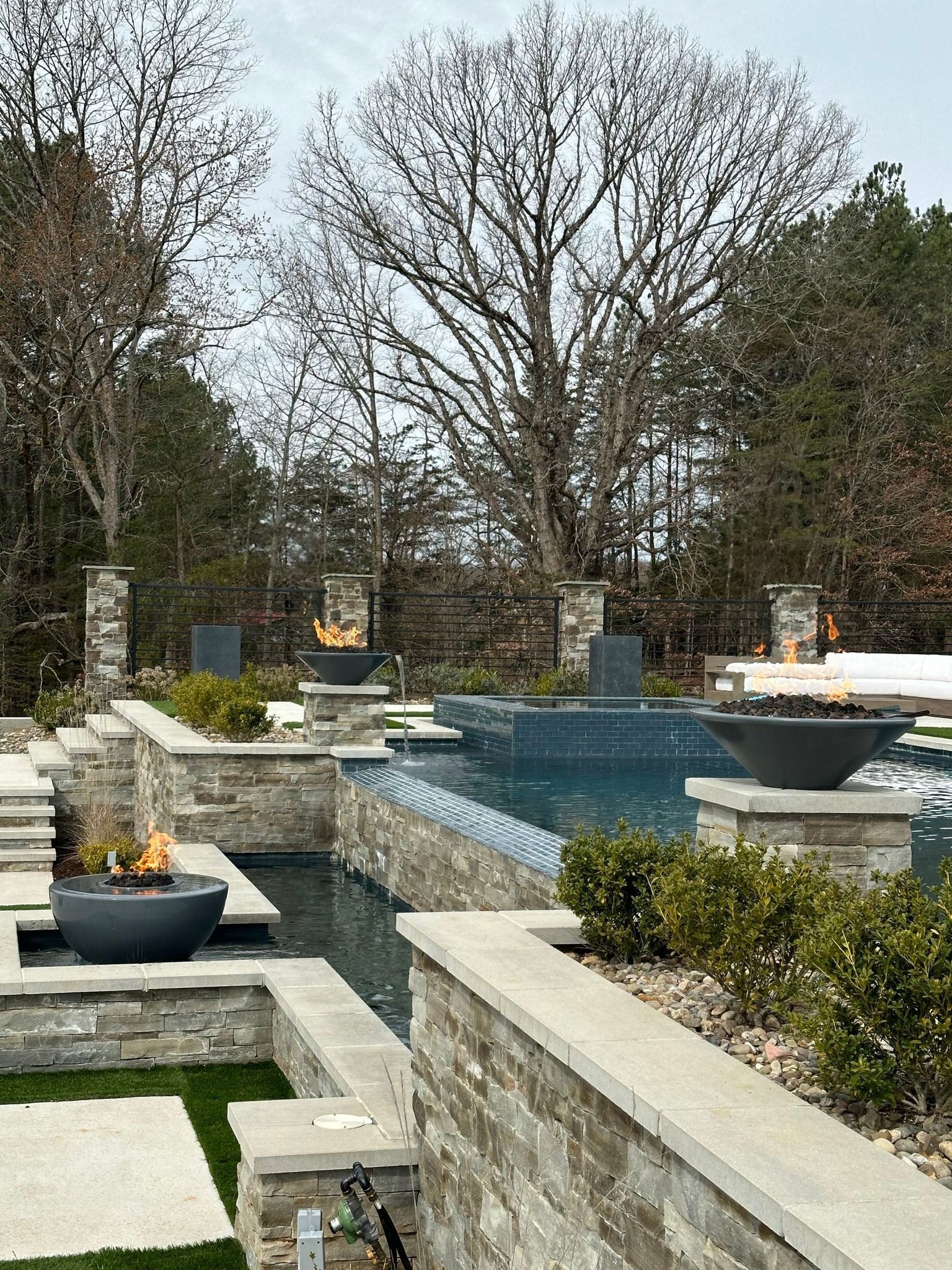 Pool area with fire bowls on stone walls, trees in the background.