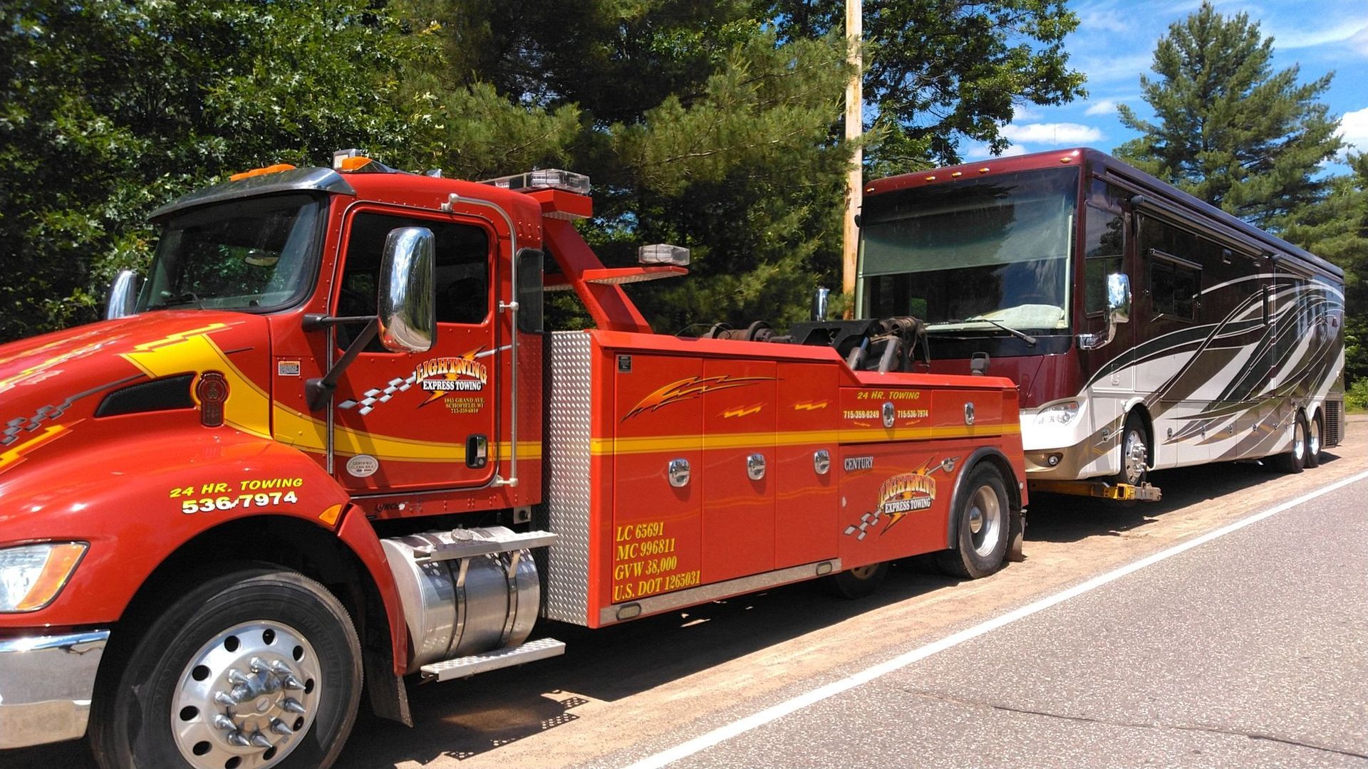 Red tow truck hauling a white and black tour bus on a tree-lined road.
