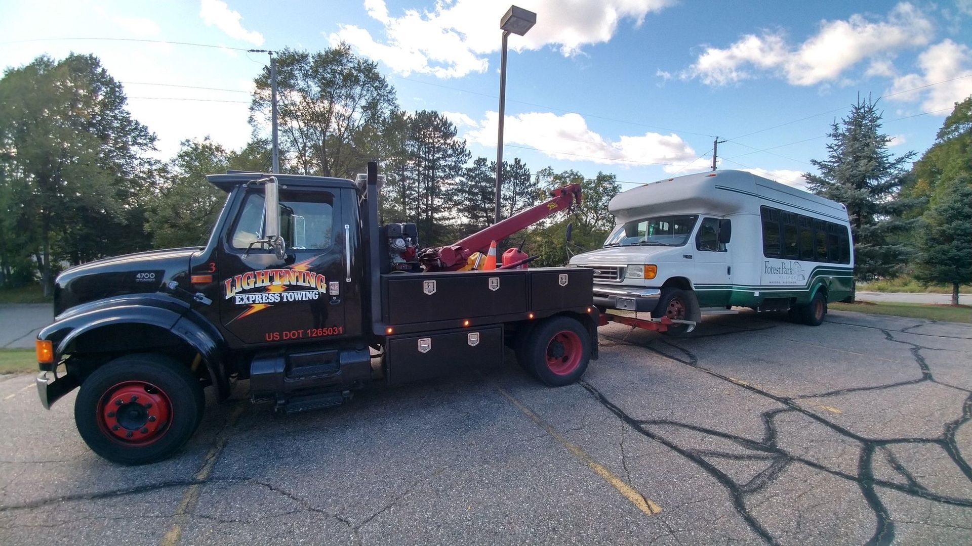Black tow truck towing a white camper trailer on a cracked parking lot under a partly cloudy sky