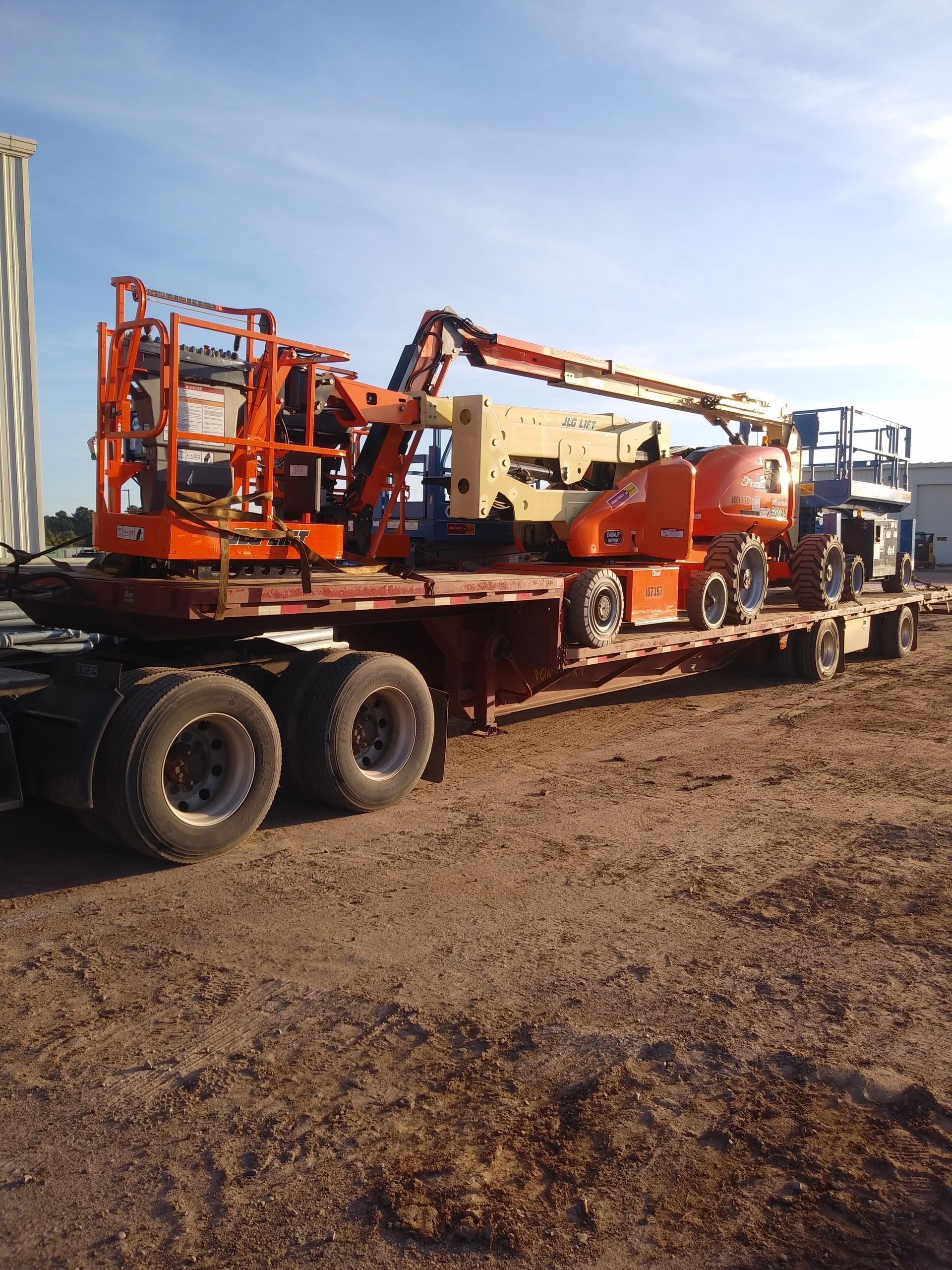 Orange drilling rig on a flatbed trailer in a dirt lot under a clear sky.