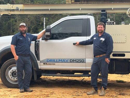 Two workers standing beside a white utility truck with a boom lift in an outdoor yard