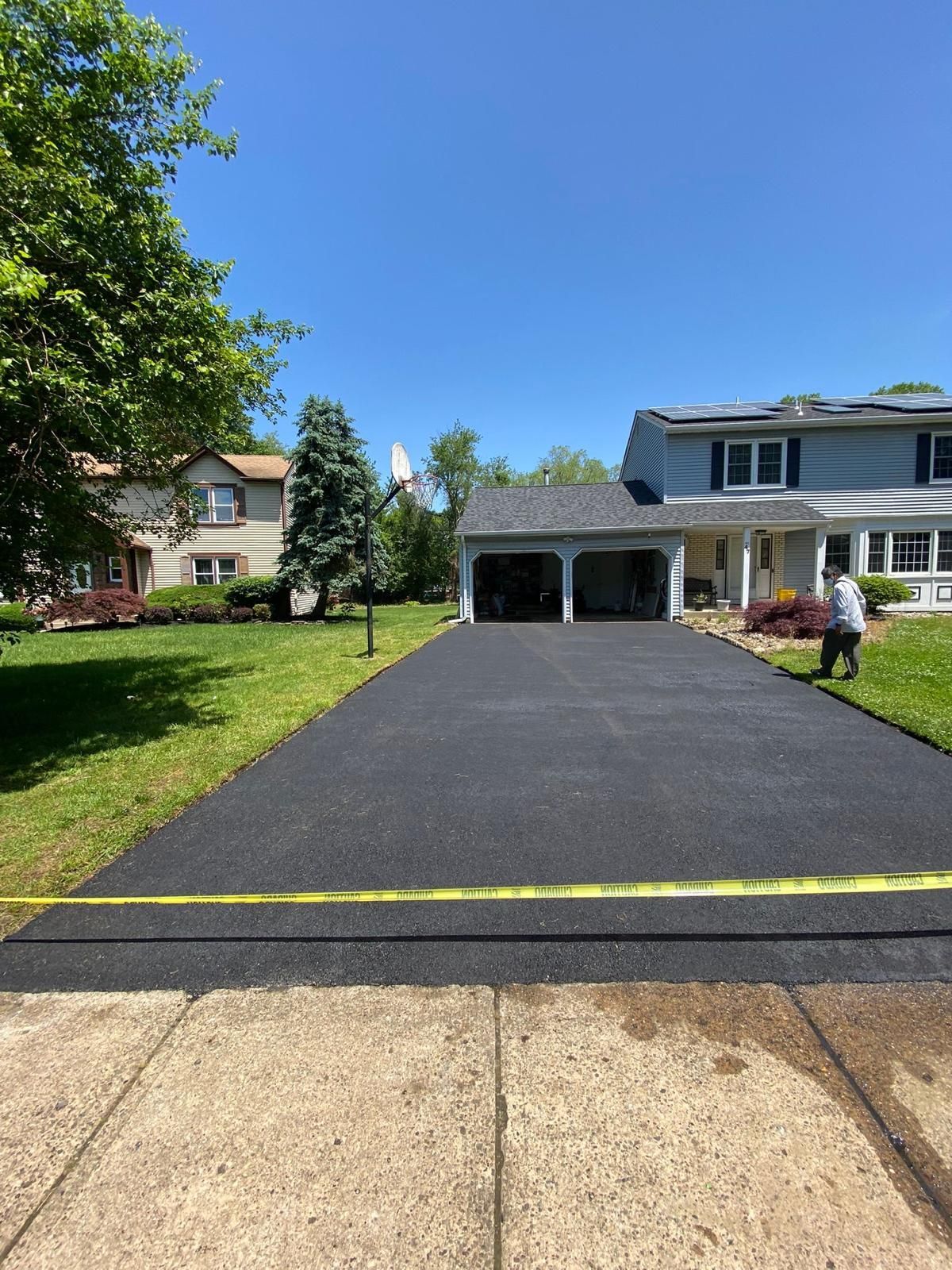 A man is walking down a paved driveway in front of a house.