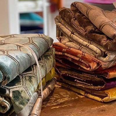 Stacks of colorful patterned velvet fabric rolls on a wooden surface.