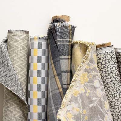 Rolled bolts of patterned fabric in various colors and textures, including gray and yellow.