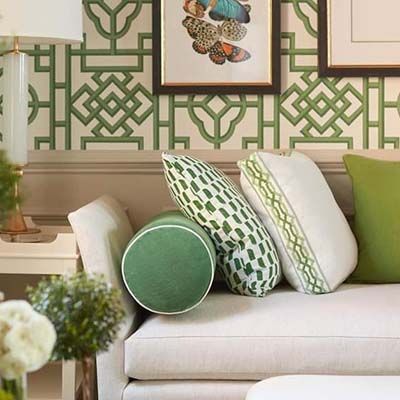 Couch with green pillows against a wall with green trellis wallpaper and framed art.