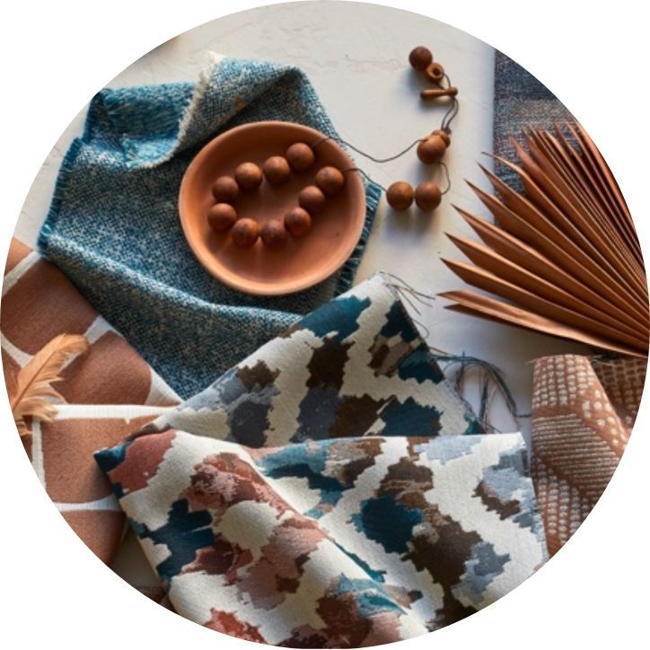 Textile swatches in teal, brown, and cream with a terracotta plate of spheres, and a dried palm frond.