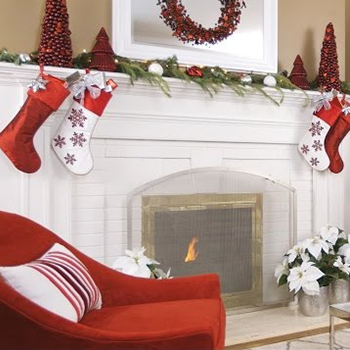 Christmas mantel decorated with red and white stockings, garland, and trees. Fireplace with a lit fire.