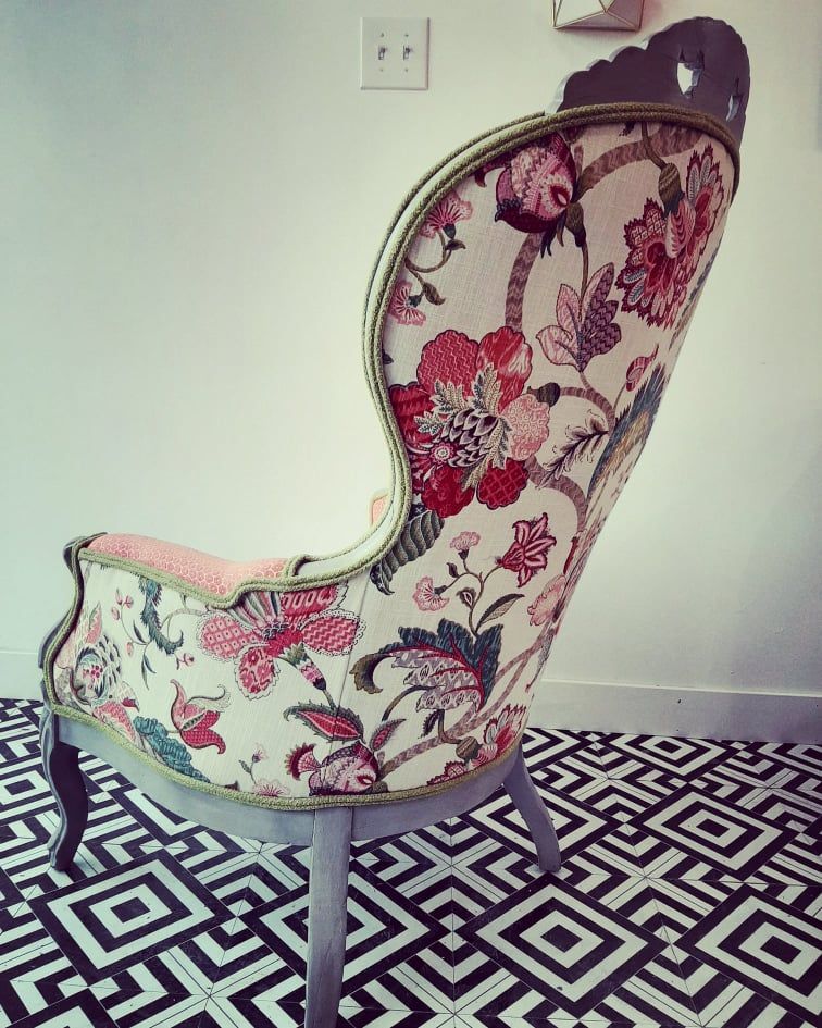Wingback chair with floral fabric on black and white geometric patterned floor.