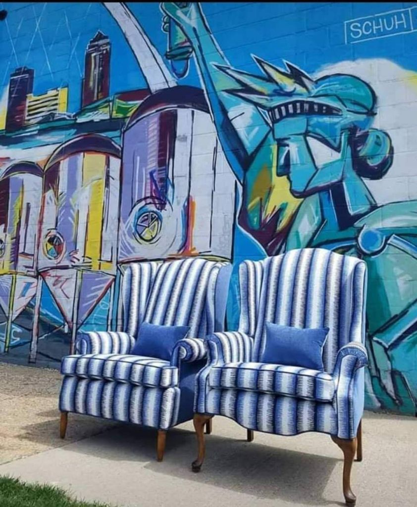 Two blue striped wingback chairs with blue pillows in front of a blue mural of a city and Statue of Liberty.