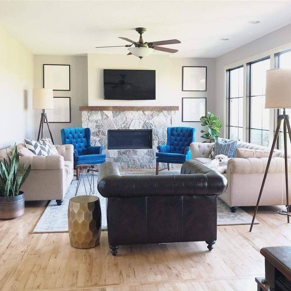 Living room with light wood floors, sofas, blue chairs, fireplace, TV, and large windows.