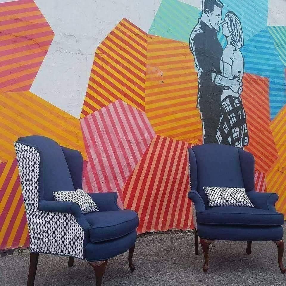 Two blue armchairs in front of a colorful wall mural with a couple kissing.