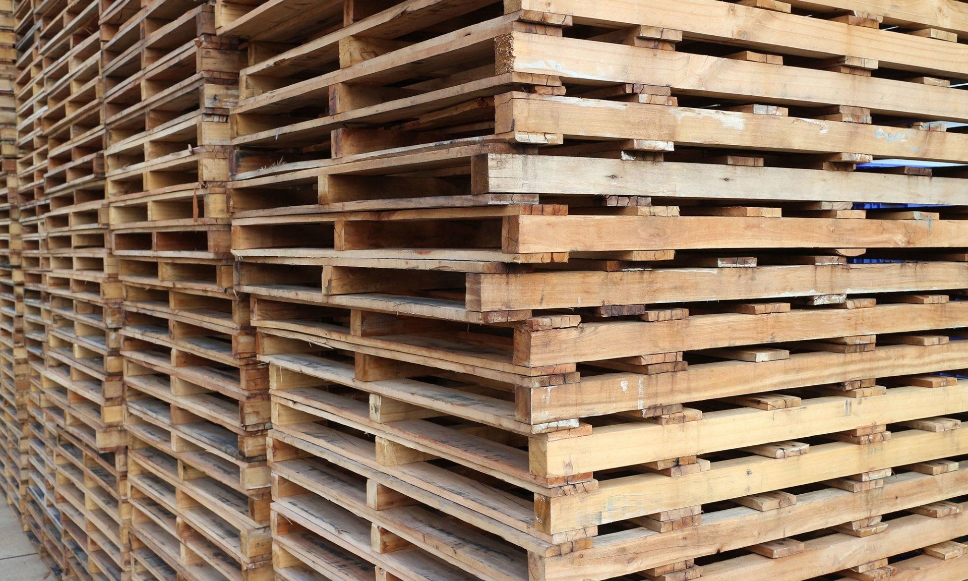 Stacks of weathered wooden pallets arranged outdoors in rows