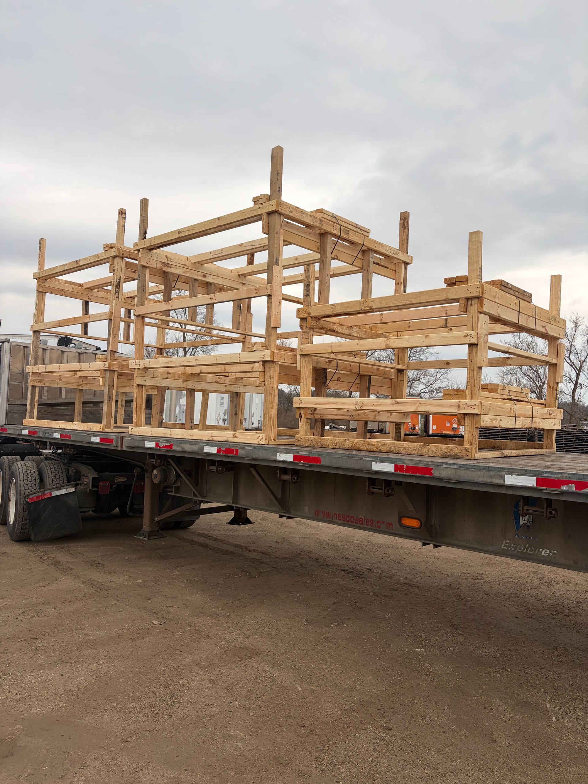 Wooden frame structure on a flatbed truck at a construction site under a cloudy sky