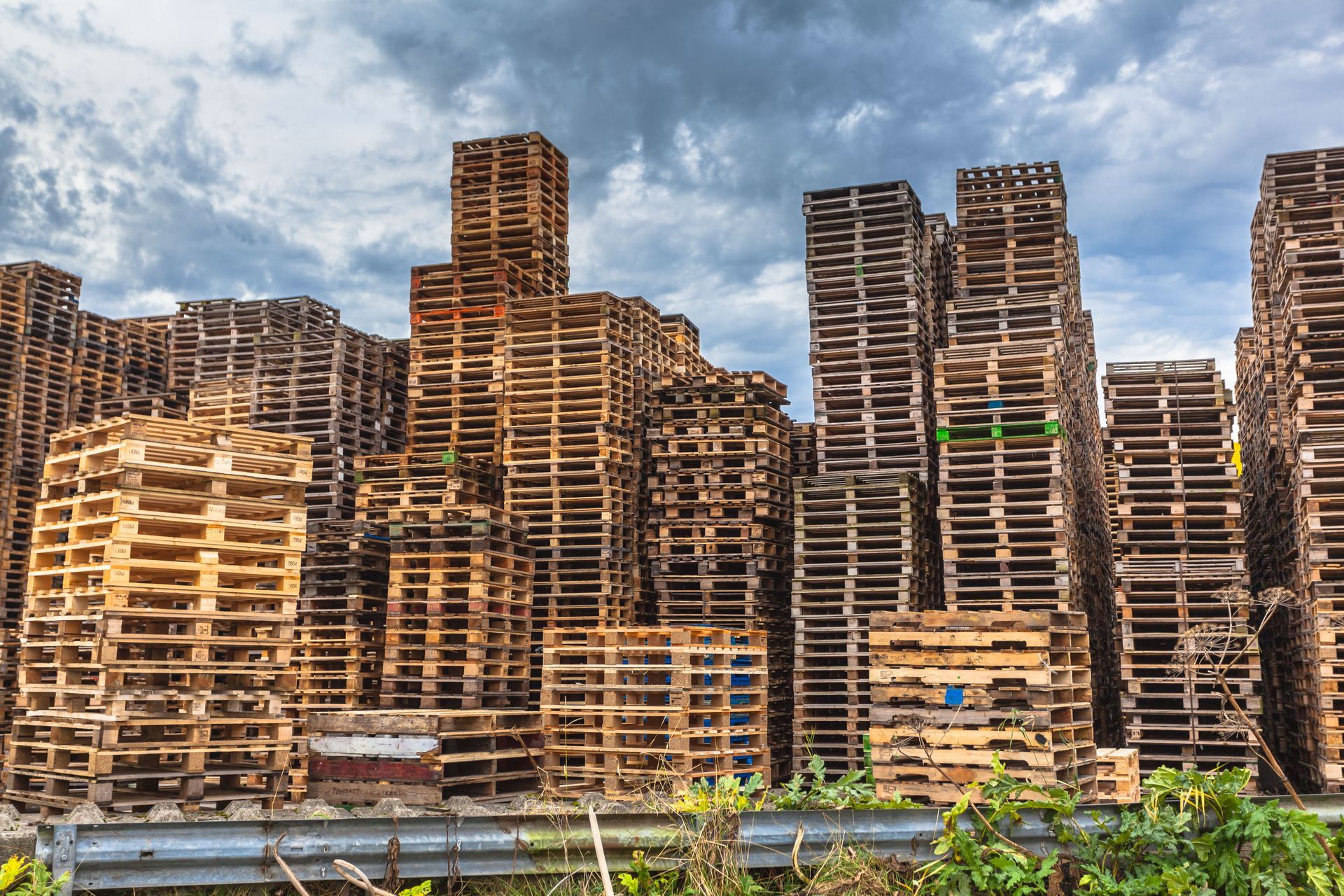 Stacks of wooden pallets forming a dense urban wall under a cloudy sky.