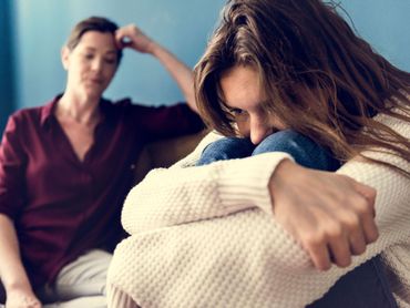 A woman is sitting on a couch talking to a depressed woman.