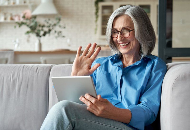 Happy, mature woman waving a hand holding a digital tablet